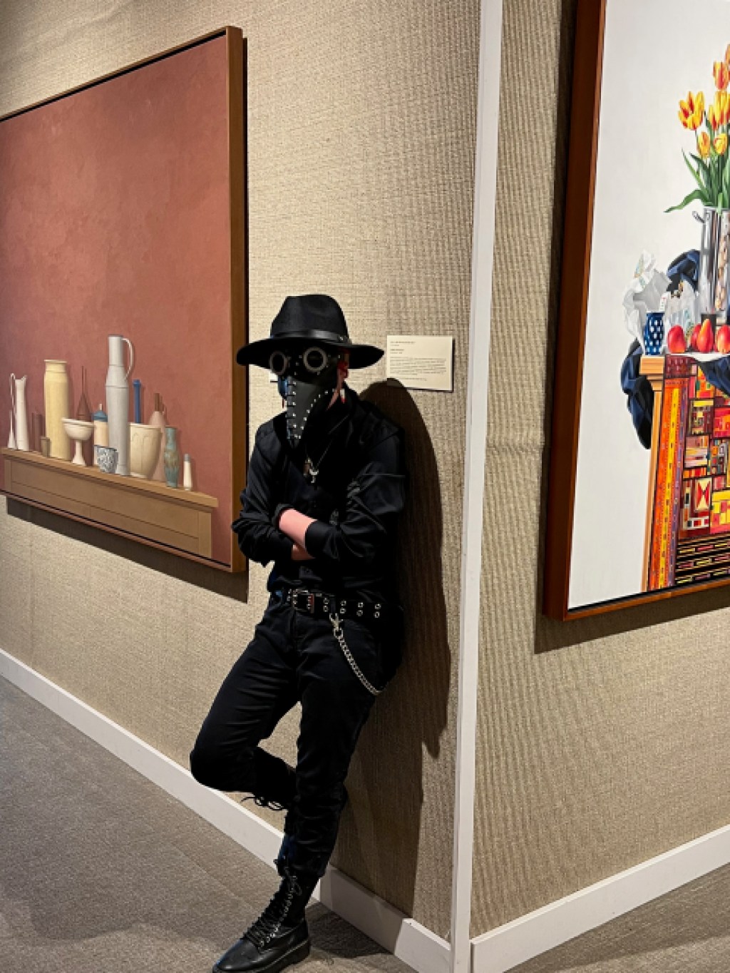 A person standing between two paintings in a museum gallery wearing a steampunk costume with a plague doctor mask