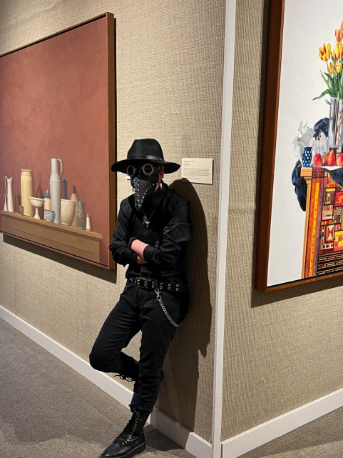 A person standing between two paintings in a museum gallery wearing a steampunk costume with a plague doctor mask