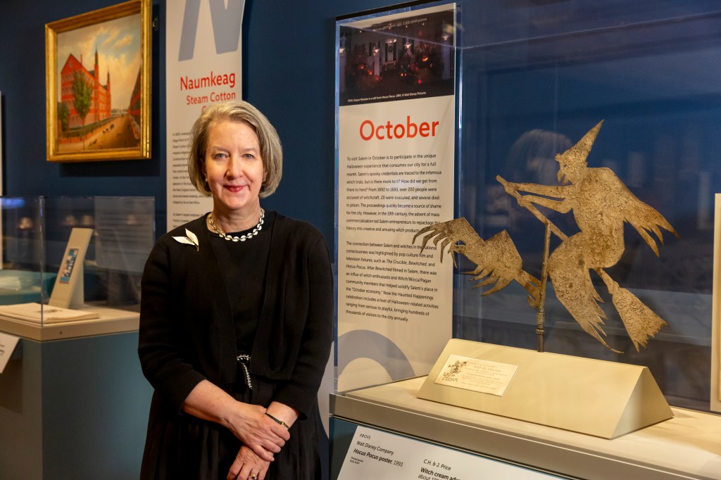A person standing in front of a witch-shaped decorative ornament in a museum gallery