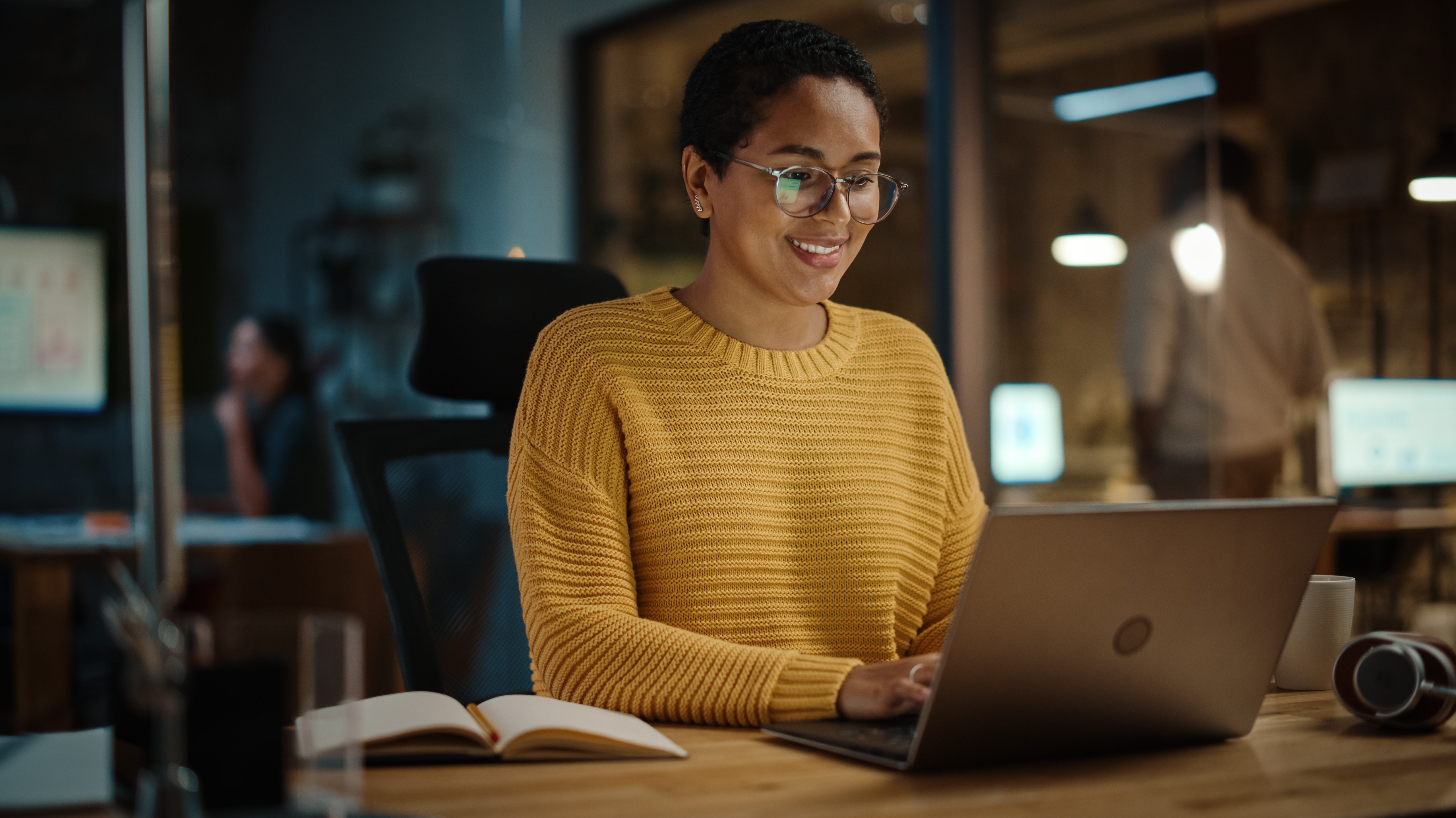 A person of color smiling while sitting in front of a laptop