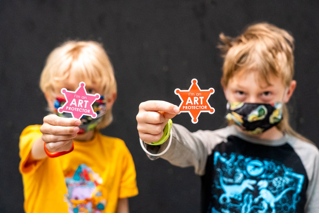 Two children holding up badge-shaped stickers that say "I'm an Art Protector"