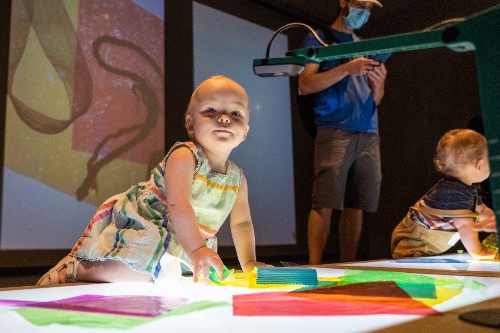 Two children crawling on a backlit surface covered with swatches of textiles