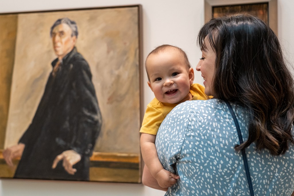 An adult and young child in a gallery in front of a portrait painting