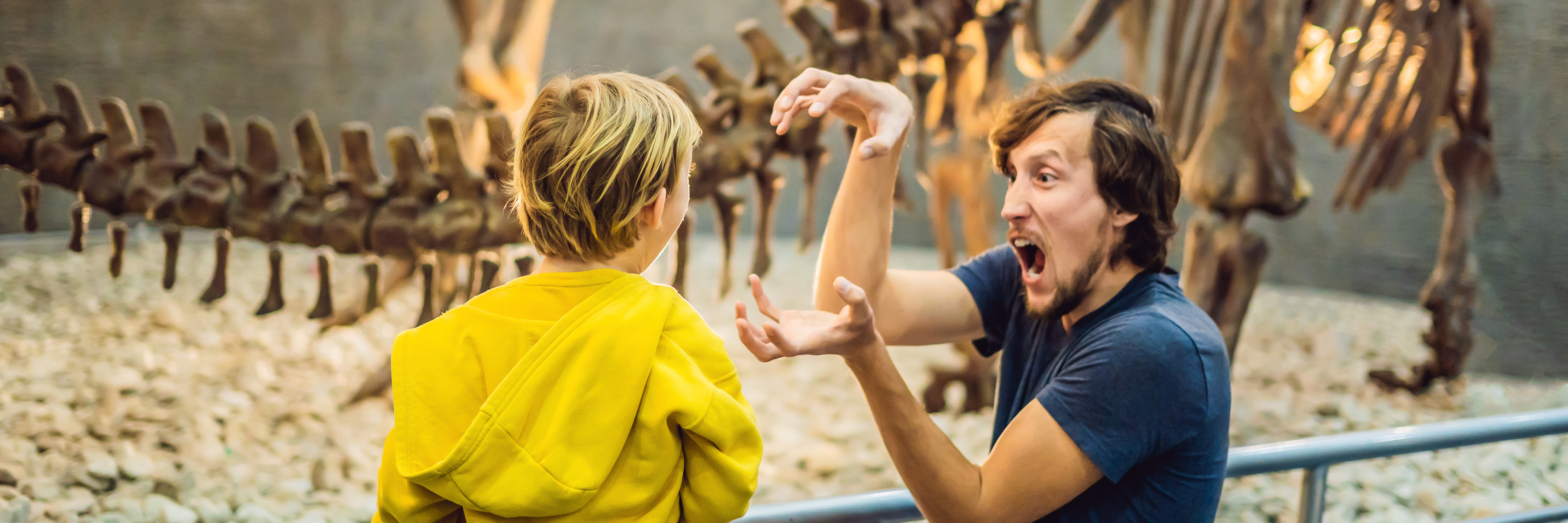 A photo of an adult imitating a dinosaur to a child in a museum exhibit 