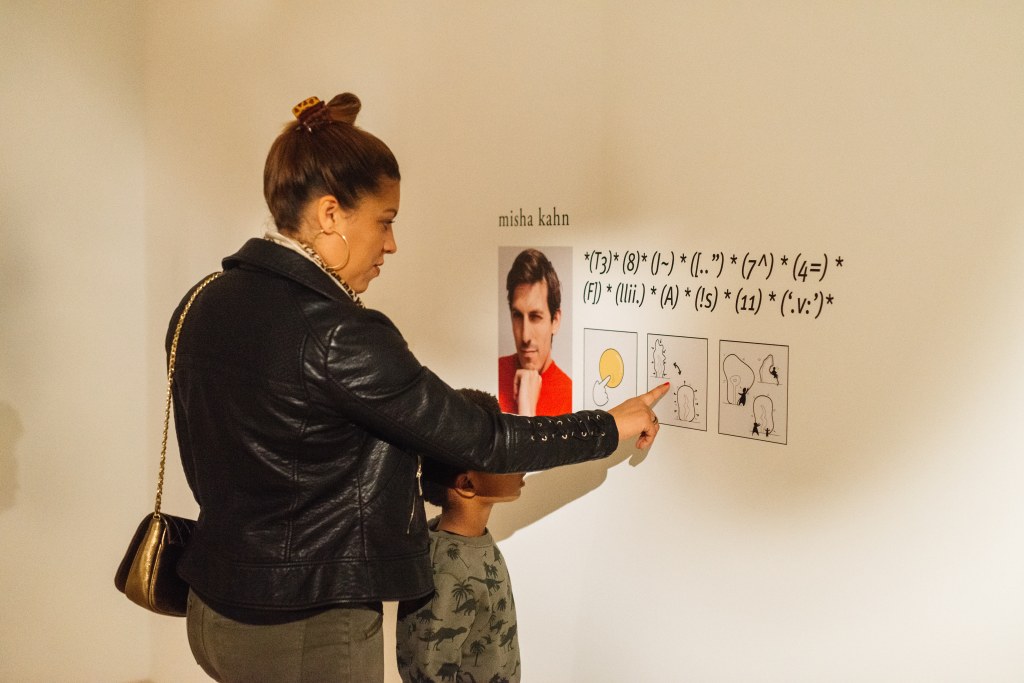 An adult and child looking at graphics on a gallery wall with a portrait and name next to mathematical equations and symbols