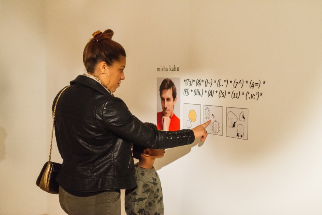 An adult and child looking at graphics on a gallery wall with a portrait and name next to mathematical equations and symbols