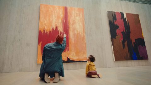 A young child and adult kneeling on the floor of a museum gallery looking at a large abstract painting