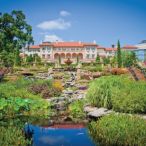 A faraway view of a large Spanishesque mansion with an abundant garden in the foreground. 