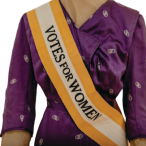 A purple silk dress with a Votes for Women sash in gold and white.