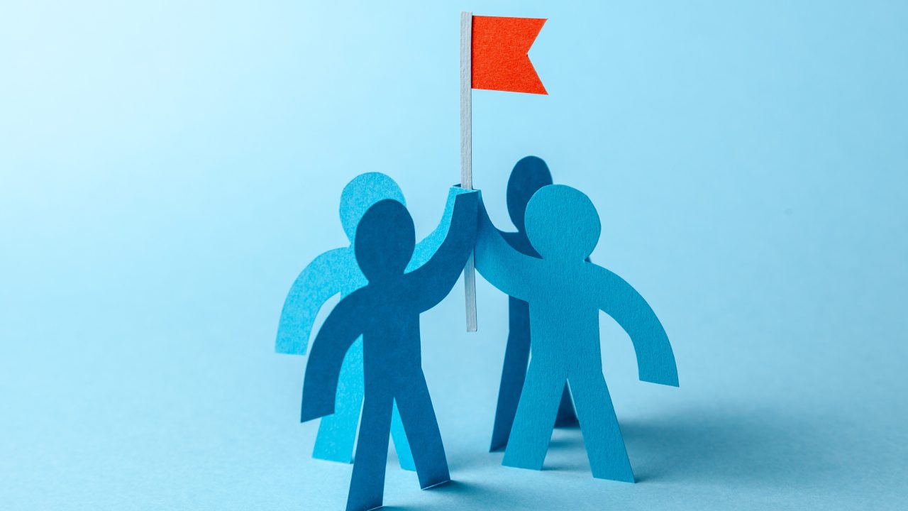 A group of paper cutout figures holding onto a red flag