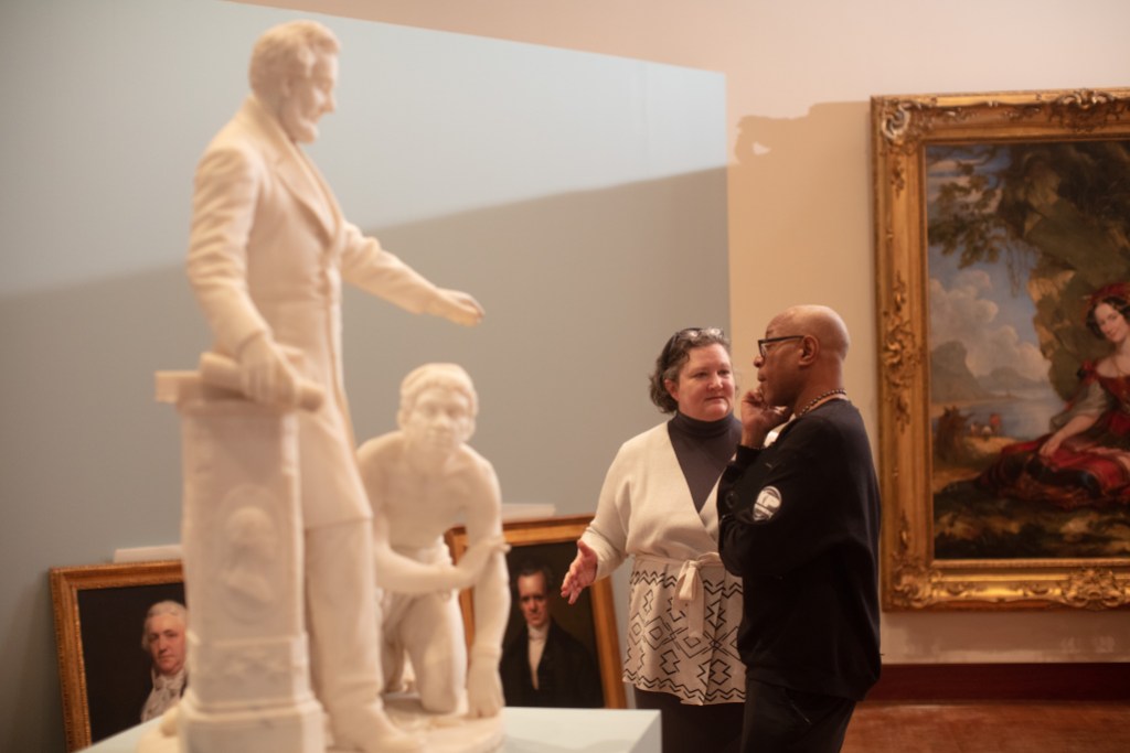 Two people talking behind a sculpture of Abraham Lincoln standing next to a kneeling figure
