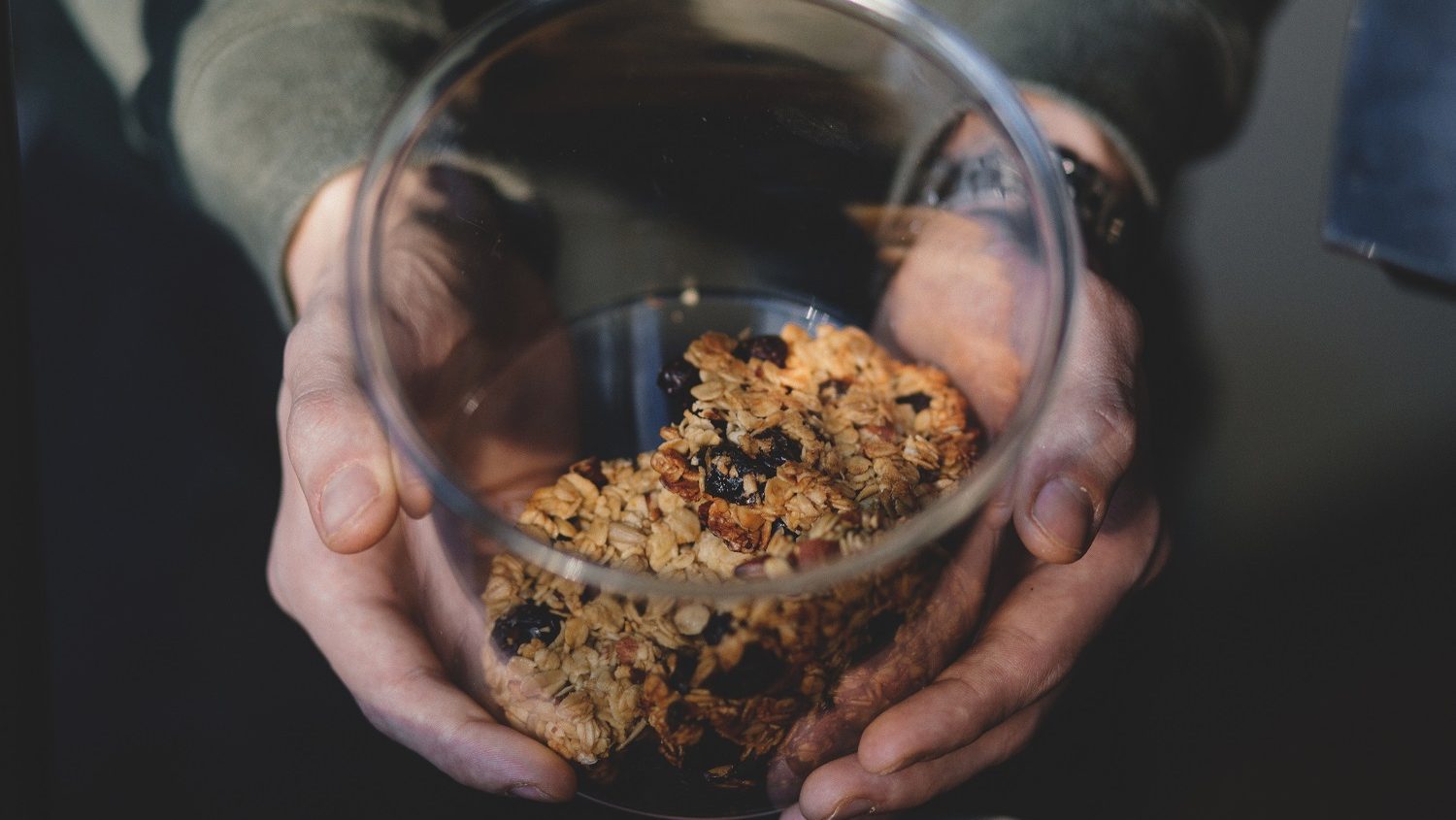 Photo by Joanna Malinowska from Freestocks.org. Image of a pair or hands holding a clear glass cookie jar with what look like oatmeal and raisin cookies inside. Shot taken from above looking down into the jar at an angle.