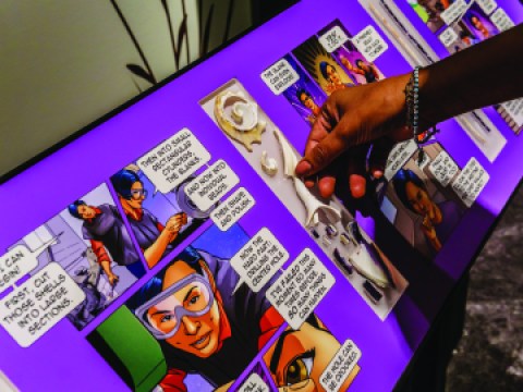 A visitor manipulates an exhibit feature with what look like comic book characters in an exhibition.
