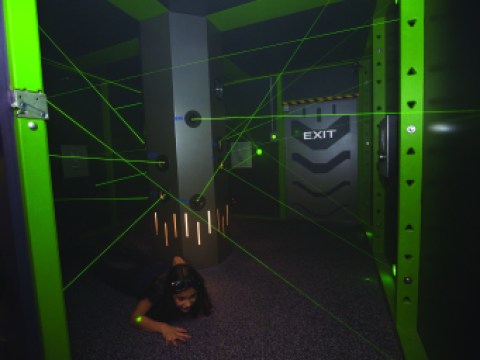 A young woman slides on her stomach under green lasers.