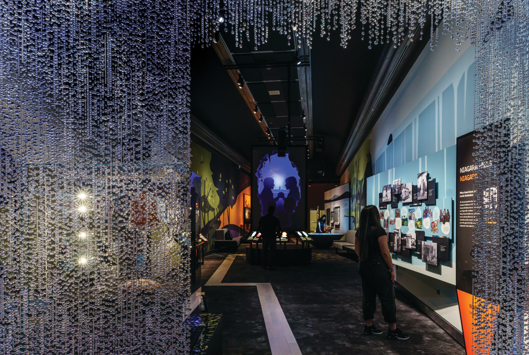 Looking into an exhibition from the entrance with images on the walls and a curtain of crystal jewels at the door.