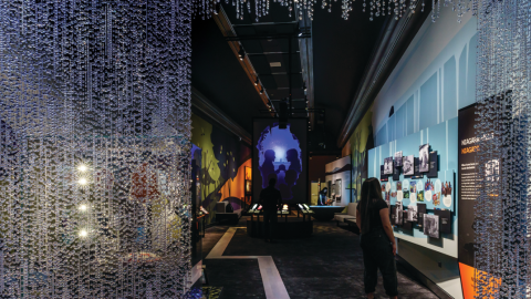 Looking into an exhibition from the entrance with images on the walls and a curtain of crystal jewels at the door.