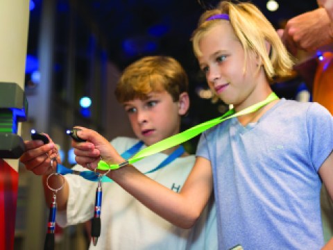Two young children hold lanyards up to a key entrance to an exhibit.