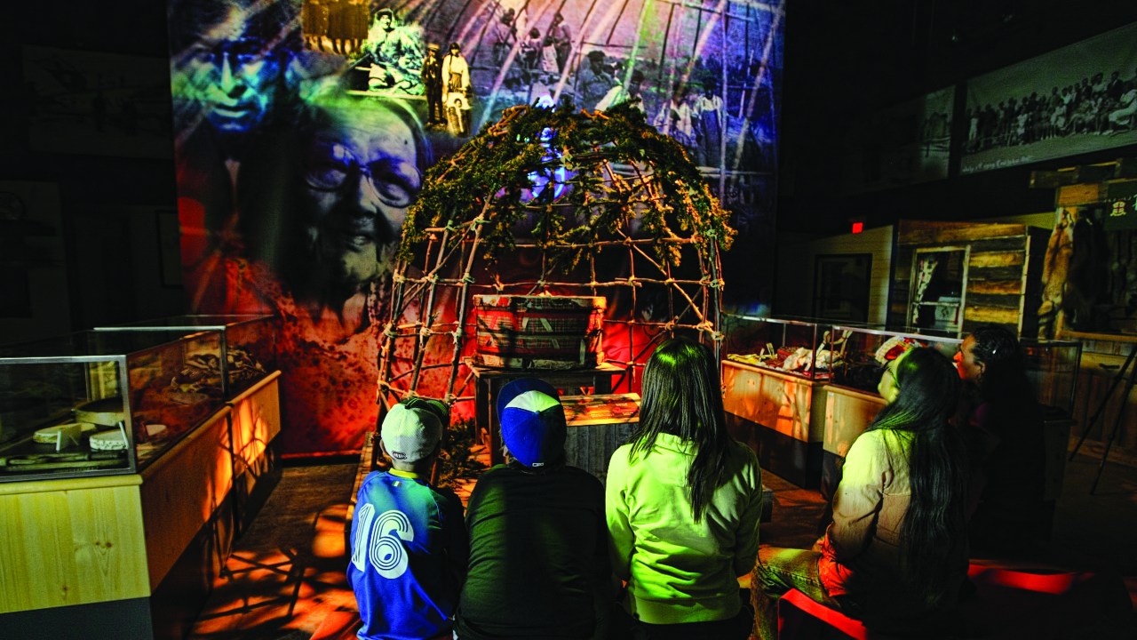 A group of people sit on their knees with their backs to the camera watching a visual display in front of them.