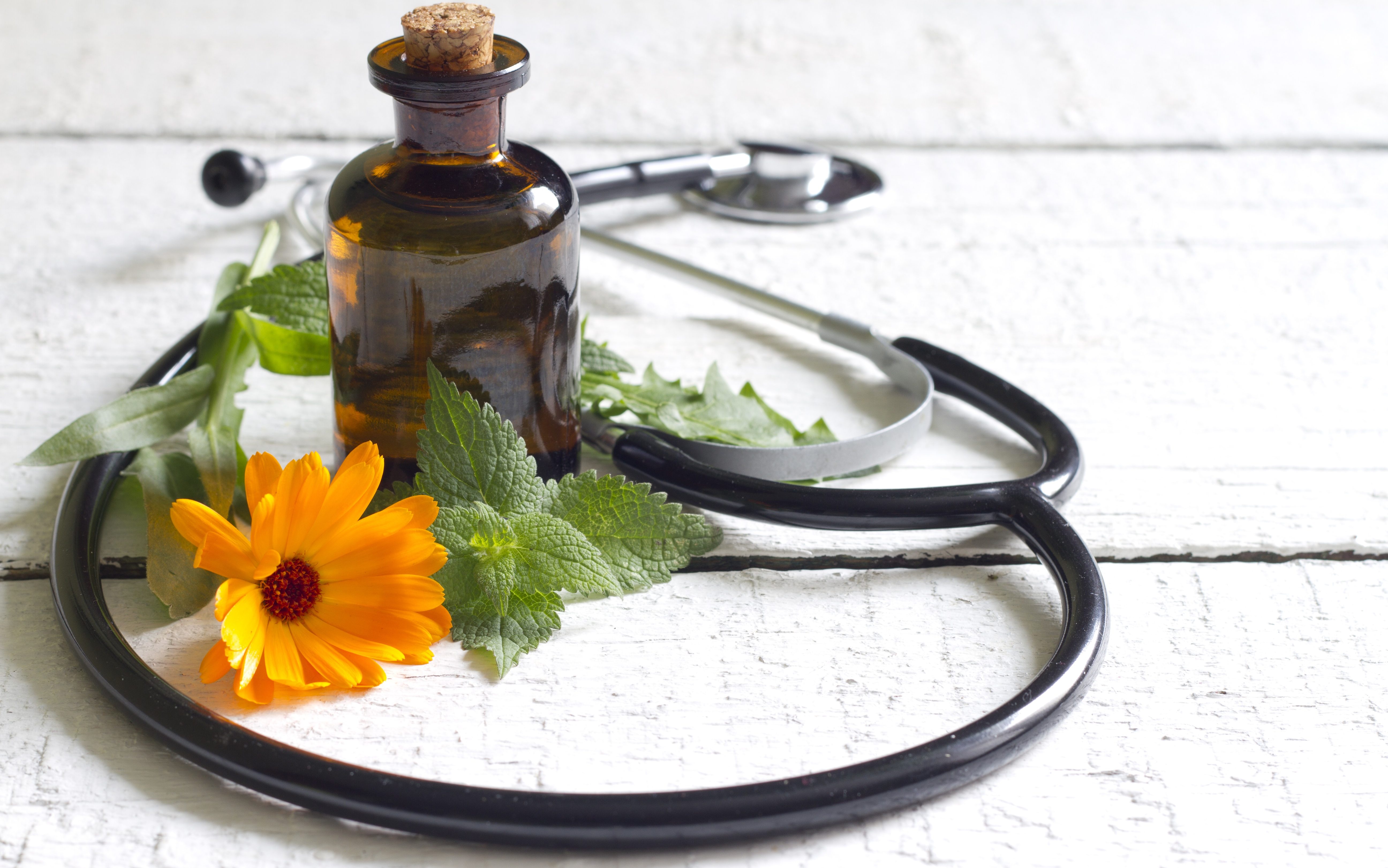 A stethoscope laying on a wooden table with a flower and brown glass jar.