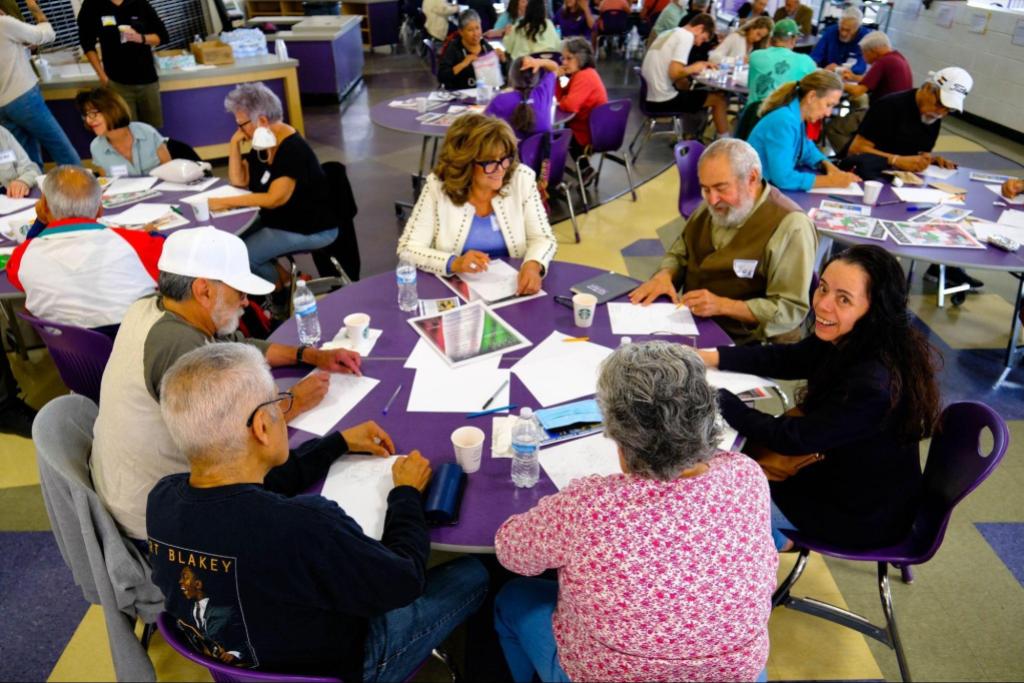 A group of people sitting at a circular table writing on pieces of paper
