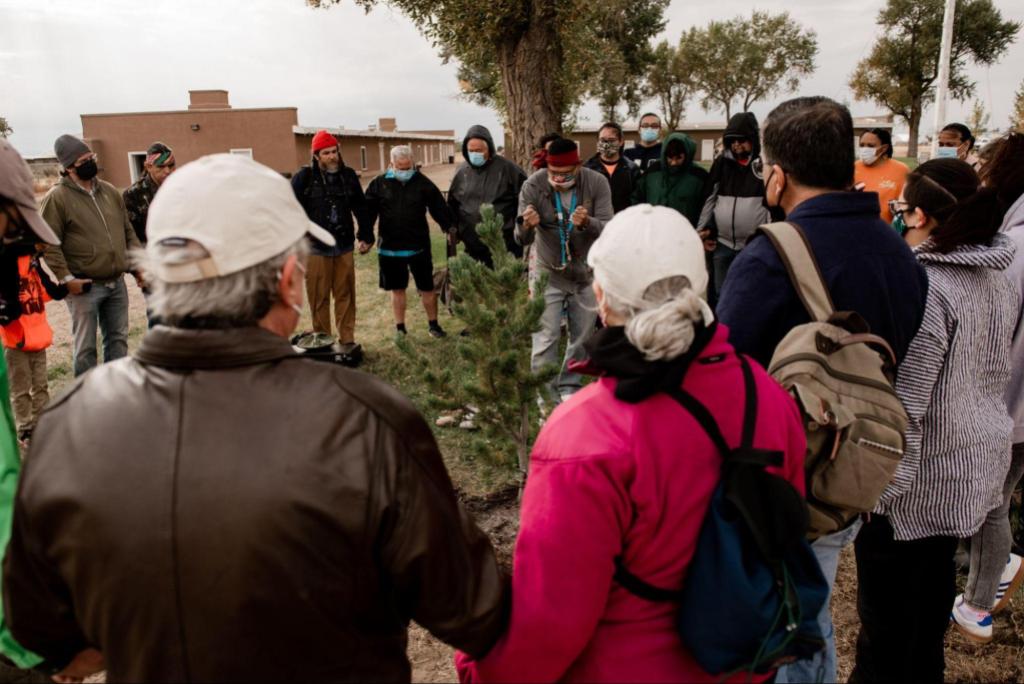 A circle of people standing around a person saying a blessing to a tree