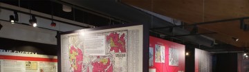 Photo of an exhibition - including display cases and a wall of map infographics