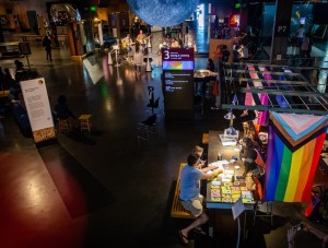 image of an exhibition from above, there is table for activities, a sign that reads Seeing & Listening, a globe hangs, and other activities (musicians are playing guitars) in the distance in the room