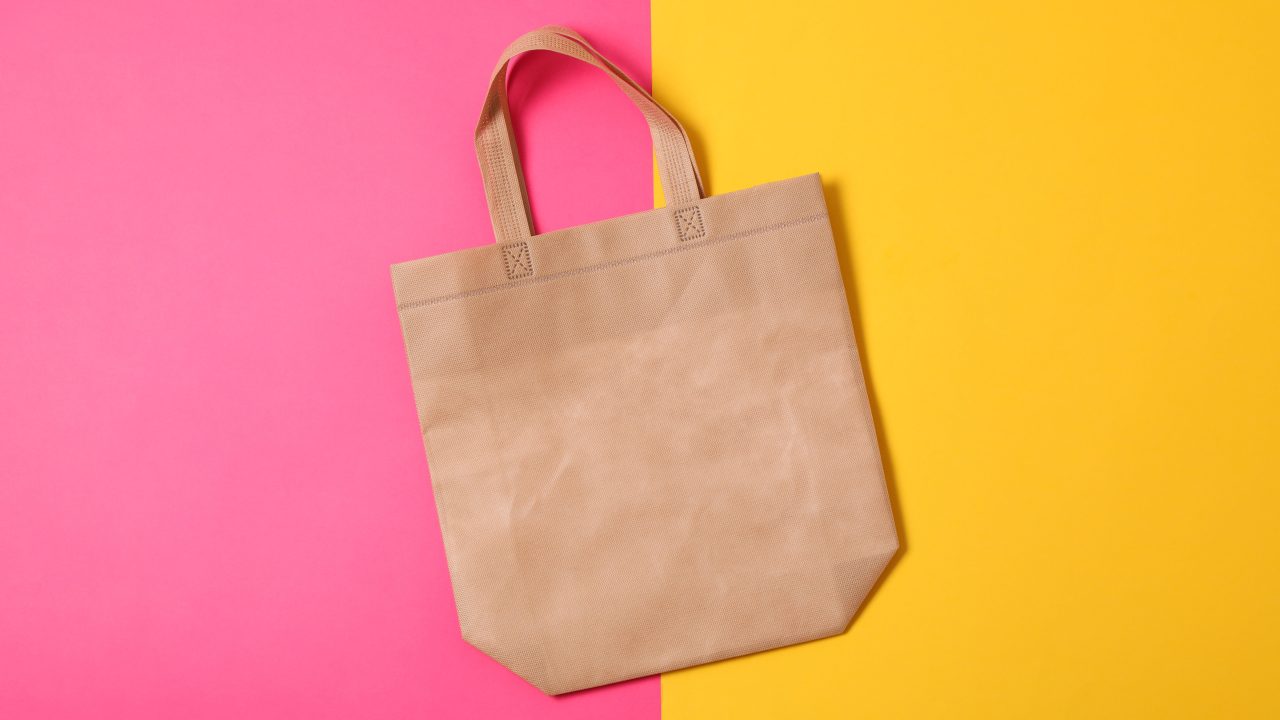 A reusable bag shown on a split pink and yellow background