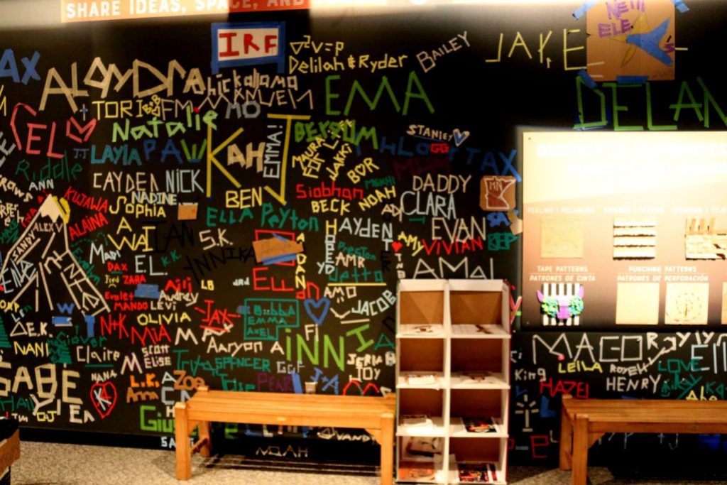 A black wall has dozens and dozens of colorful tape words and symbols on it.