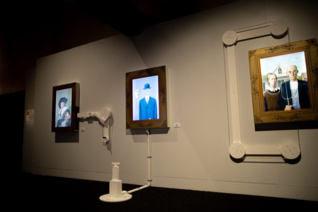 A wall with framed photographs lit from behind or within with various medical looking equipment coming from the wall. 