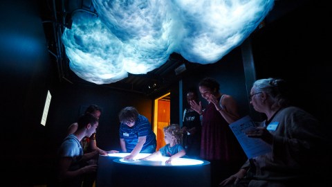 A group of children stand in a circle looking at a glowing table in front of them.