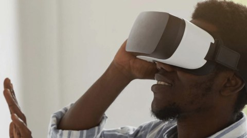 A person stands in profile wearing a VR headset with their hand outstretched toward a wall with framed images.