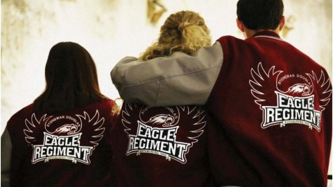 Three people stand with their backs to the camera with red letterman jackets on that say Eagle Regiment with a spread eagle embroidered on them.