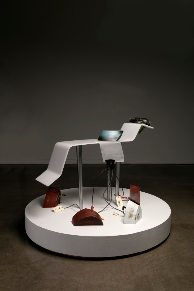 A sculptural artwork consisting of a reclining chair with a speaker on the headrest and a node of wires connected to plinths with the names of Indigenous tribes on them