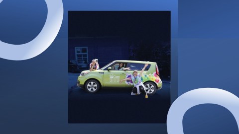 Three people stand behind, in front of, and inside a small green car decorated with Van Gogh art.