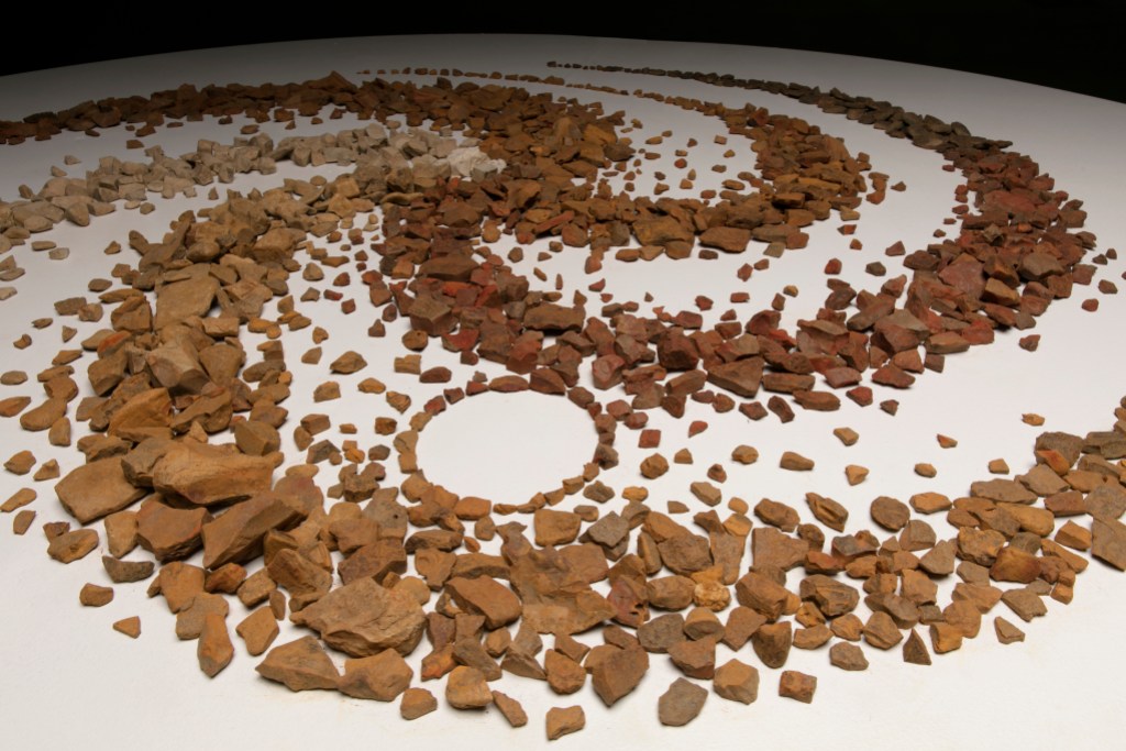 An installation artwork consisting of red-brown rocks arranged in a spiral pattern