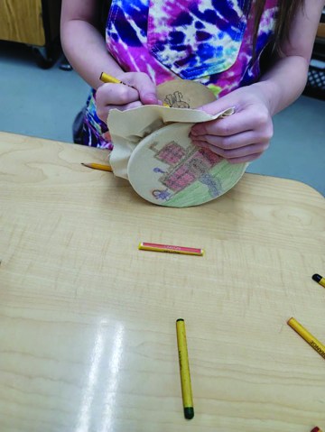 A child's hands making a paper decoration at a wooden table. 
