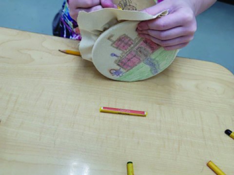 A child's hands making a paper decoration at a wooden table. 