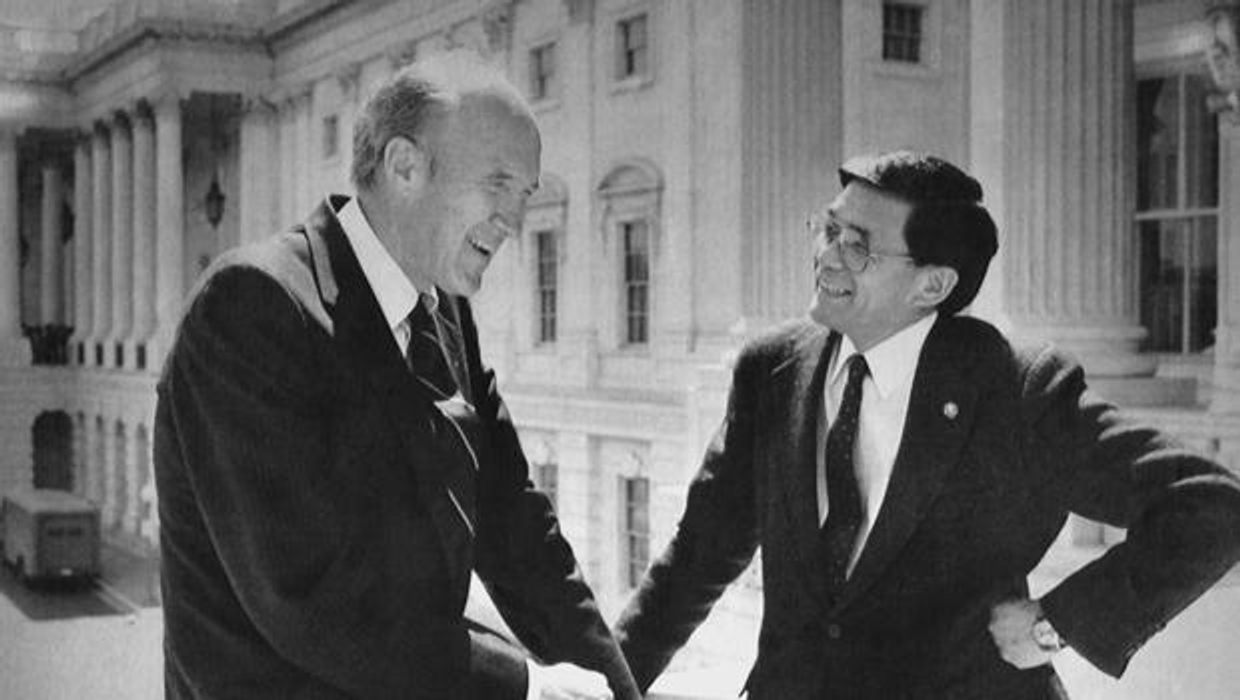 A black-and-white photo of two people smiling in front of a neoclassical building