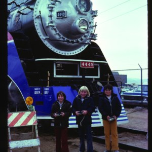Three people stand in front of the engine of a train.