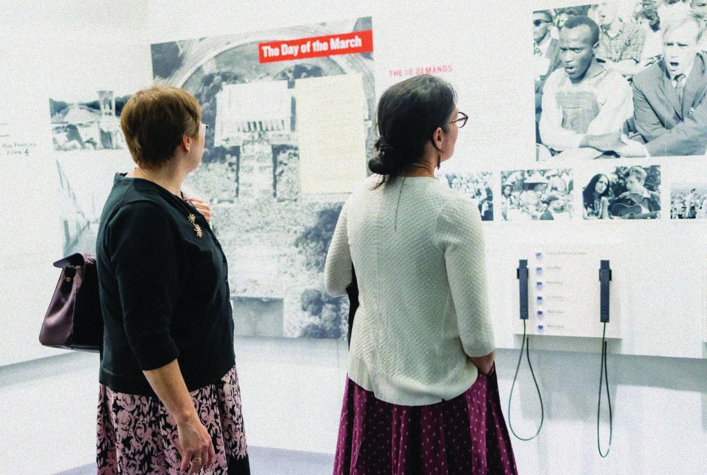 Two people stand looking at an exhibit wall.