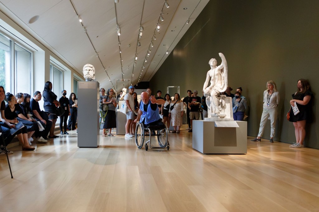 Visitors watching a performer moving through a museum gallery in a wheelchair