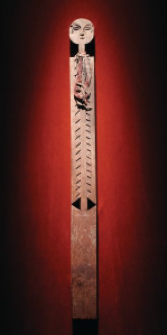 A wooden statue sits against a red background wall. 