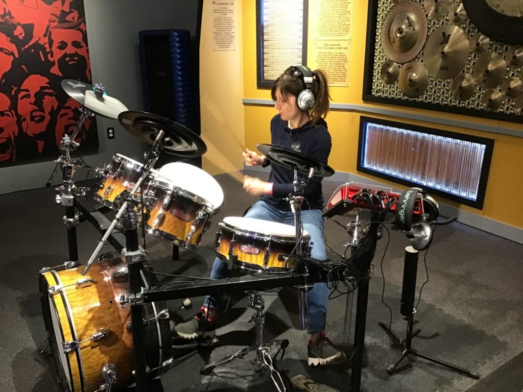 A young person sits at a drum set drumming.