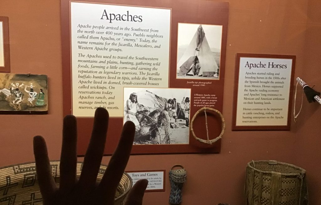 Someone places their hand on the glass of an exhibit featuring Apaches.
