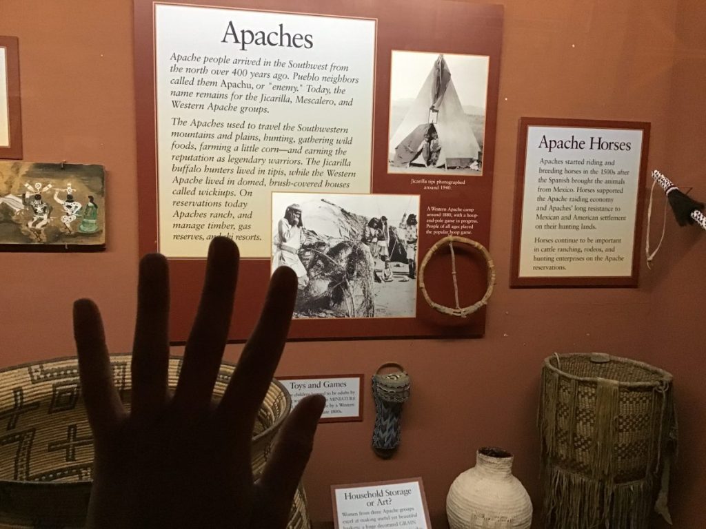 Someone places their hand on the glass of an exhibit featuring Apaches.