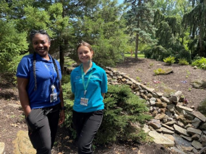 Two volunteers in blue shirts posing near a stone wall at the Rock Garden of Estate Hospital.