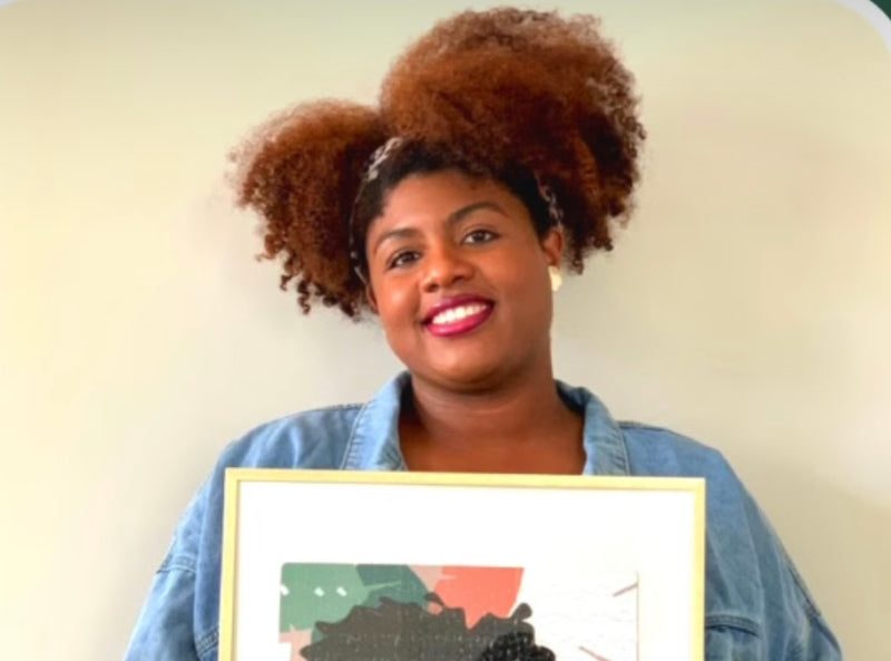 An African American woman stands holding a framed image of another African American woman.