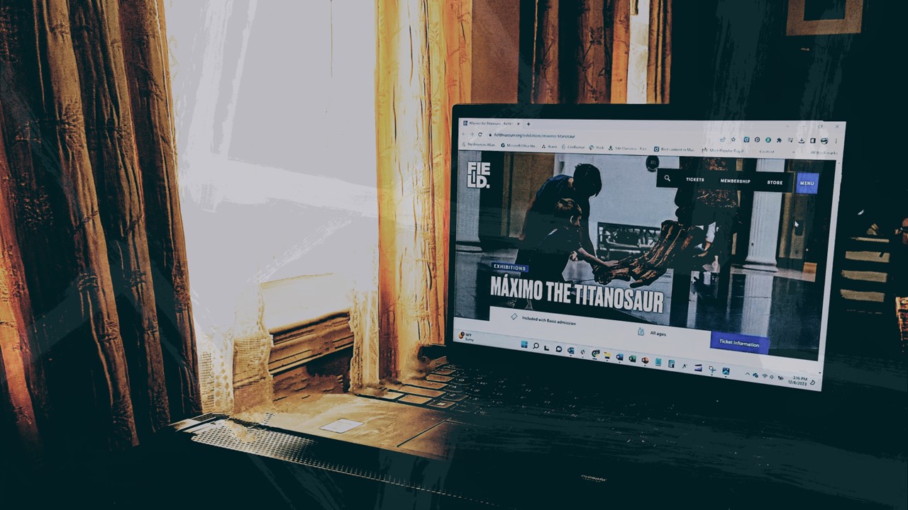 An open laptop with the Field Museum website open sits on a desk in front of a window.