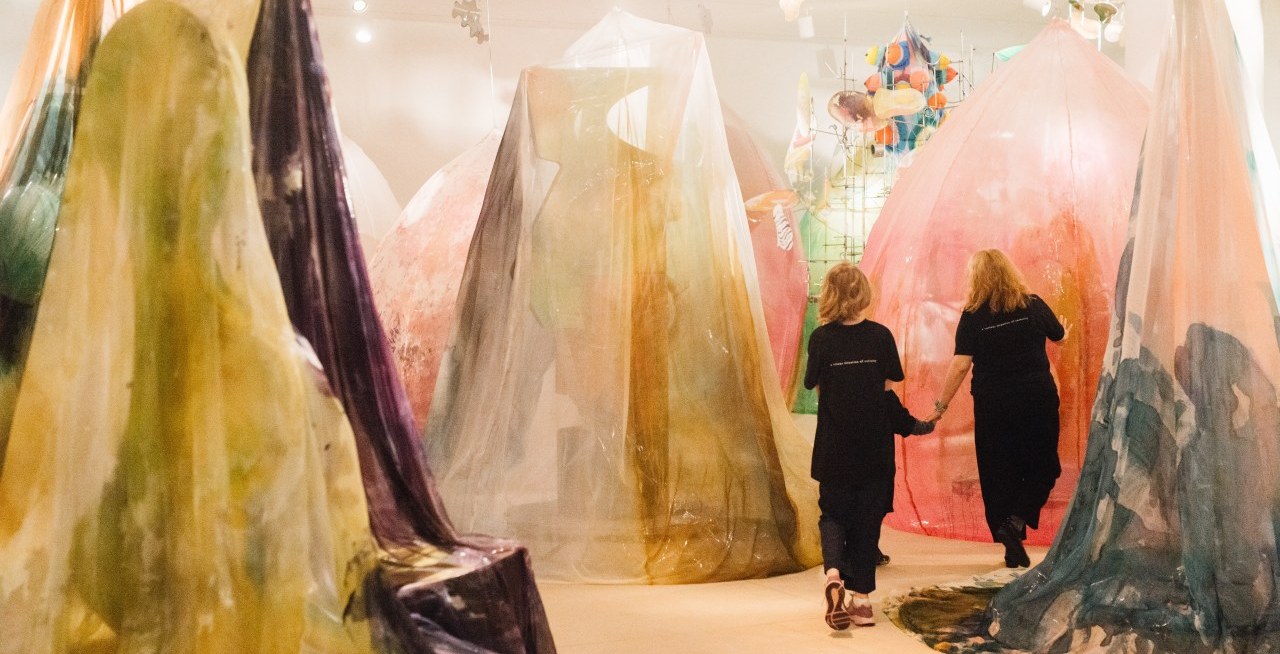 Two people walking through an installation with sculptures consisting of draped painted textiles